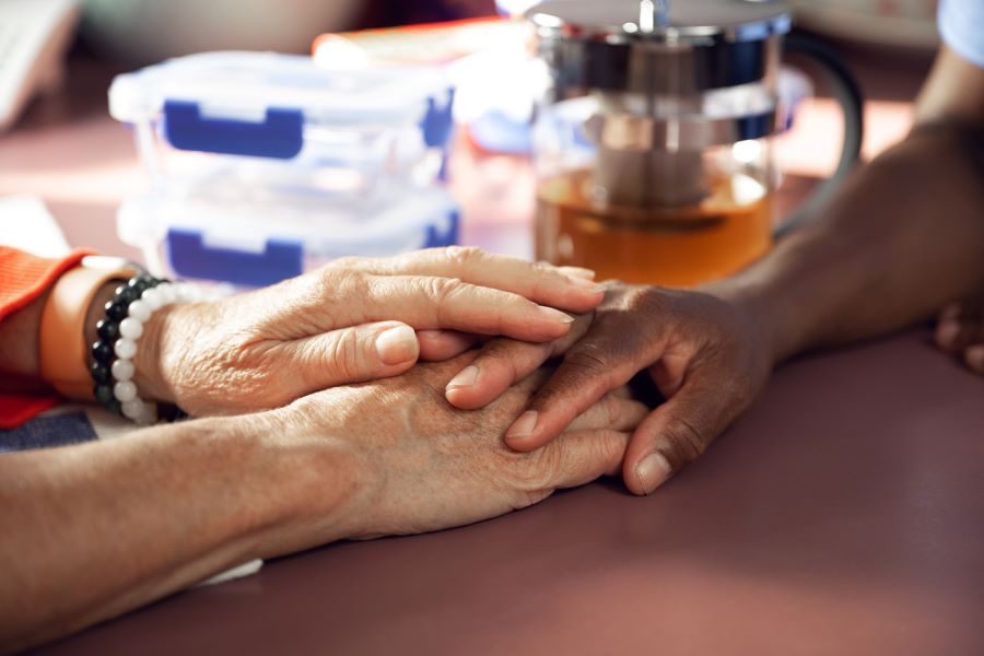 Close-up of two people holding hands on a table, with a teapot and plastic containers in the background.