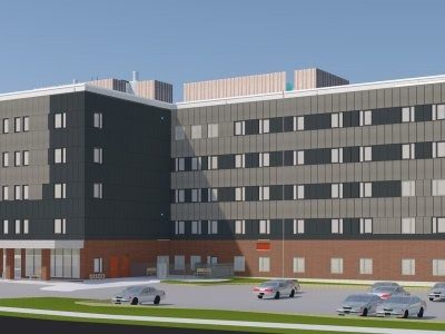 A modern, multi-story building with a brick and dark panel exterior, several windows, and parked cars in the foreground under a clear sky.