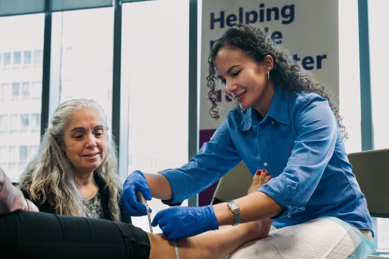 A healthcare professional wearing blue gloves examines a patient's foot while another woman observes in a clinical setting.