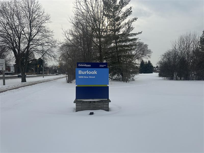 A sign for Extendicare Burloak at 9839 New Street stands surrounded by snow and trees on a cloudy winter day.