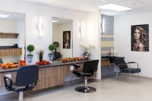 A modern hair salon with two styling chairs, large mirrors, fall-themed decorations on the counter, and a poster of a woman with wavy hair on the wall.