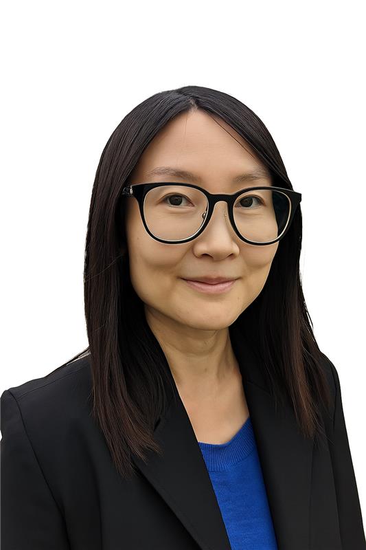 A person with straight dark hair wearing black glasses, a blue top, and a black blazer, facing the camera against a white background.