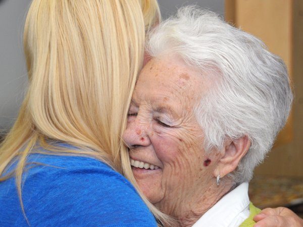 An older woman with white hair smiles while hugging a younger woman with long blonde hair.