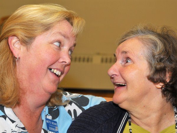 Two women are smiling at each other, appearing happy and engaged in conversation.