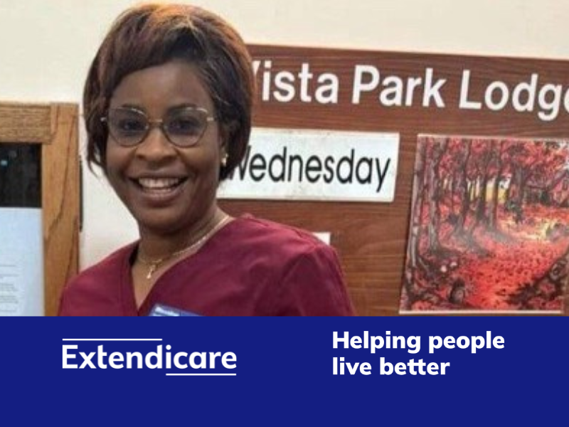 A woman wearing glasses and a maroon uniform smiles in front of a sign reading "Vista Park Lodge," a long term care home. The Extendicare logo and slogan appear at the bottom.