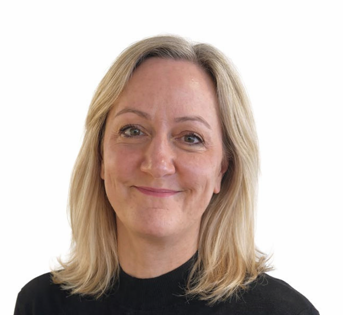 A woman with shoulder-length blonde hair and a black top smiles at the camera against a plain white background.