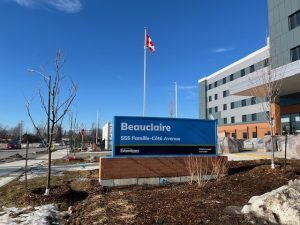 A blue sign in front of a modern building reads "Beauclaire, 555 Famille-Côté Avenue," with a Canadian flag on a pole nearby, marking the location of Extendicare Beauclaire.