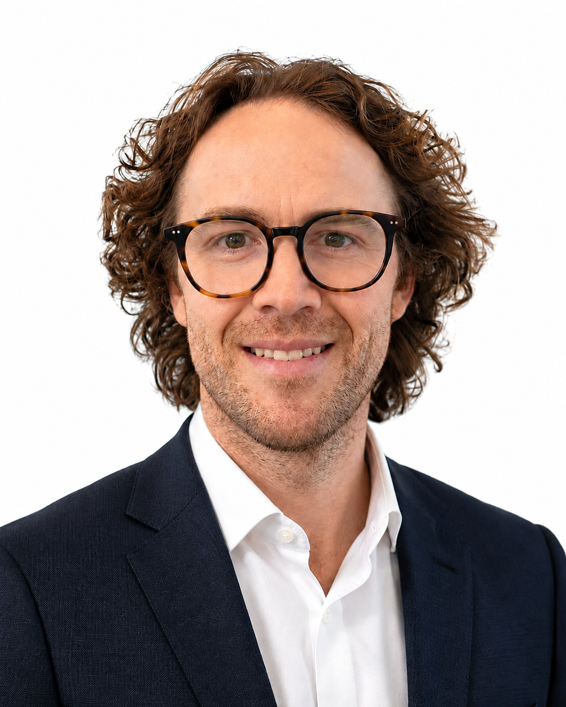 Man with curly brown hair and glasses wearing a white shirt and dark blazer, smiling in front of a plain white background, representing the professionalism of the Extendicare leadership team.
